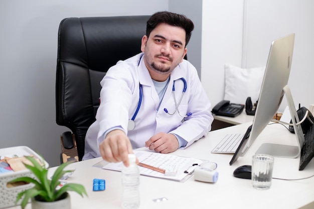 Um jovem médico está sentado na cadeira da clínica e segurando uma garrafa de água na mão