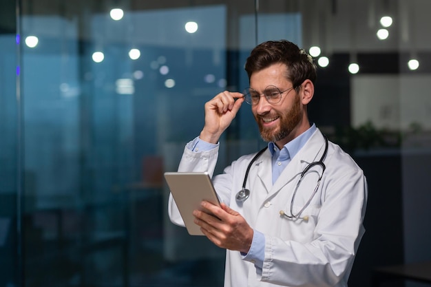 Um jovem médico estagiário estagiário está parado em um escritório em um hospital com um jaleco branco e com um