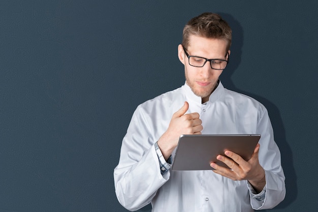 Um jovem médico segurando um tablet digital isolado em pé perto da parede colorida