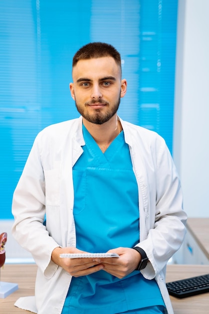 Um jovem médico sério de avental branco posa no escritório da clínica moderna Médico profissional no local de trabalho Closeup