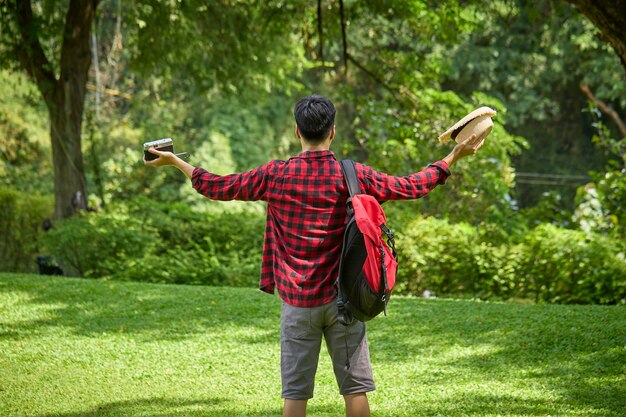 Um jovem mochileiro asiático segurando uma câmera em um parque natural.