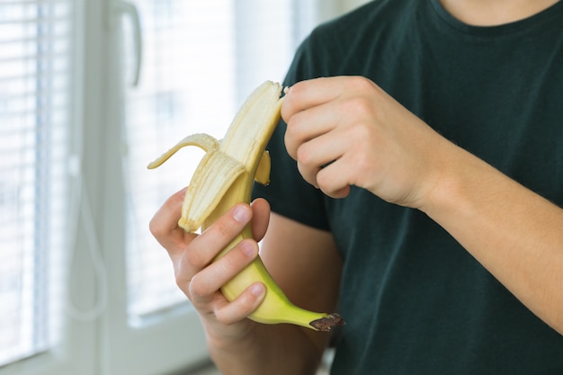 Um jovem morena bonito está de pé na cozinha em casa e limpa uma banana.
