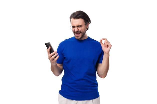 Foto um jovem moreno bem cuidado com barba em uma camiseta assiste a um vídeo em um smartphone