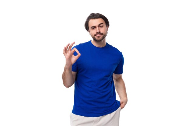 Foto um jovem moreno com barba vestido com uma camisa azul mostra um gesto de classe em um fundo branco