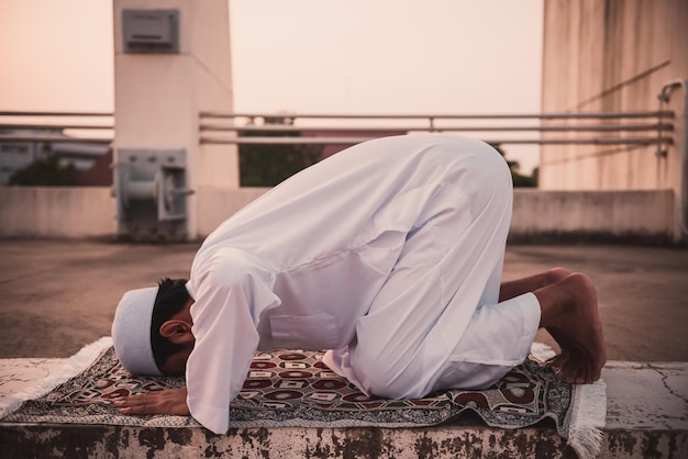 Um jovem muçulmano asiático rezando no conceito de festival do pôr do sol do Ramadã