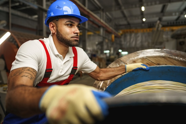 Um jovem operário de fábrica enrola uma espessa bobina de cabo elétrico