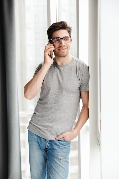 um jovem otimista feliz dentro de casa em casa falando pelo telefone celular.