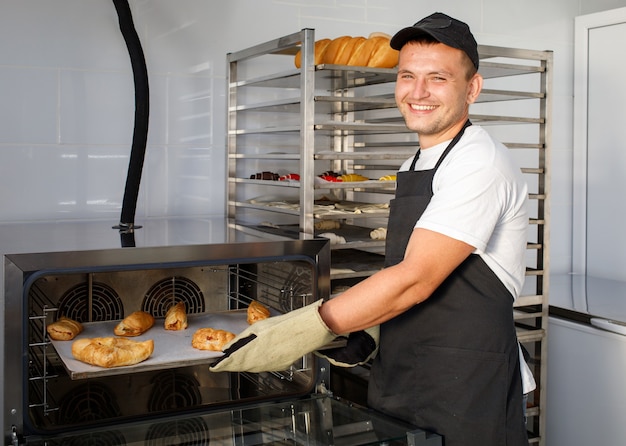 Um jovem padeiro tira os pastéis do forno na padaria