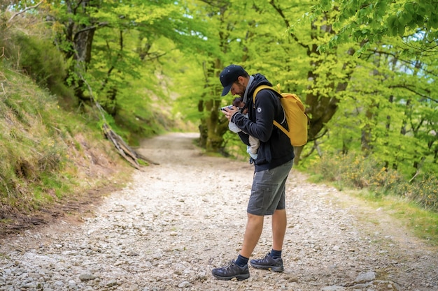 Um jovem pai colocando o filho recém-nascido bem na mochila em um caminho na floresta em direção ao piquenique com a família