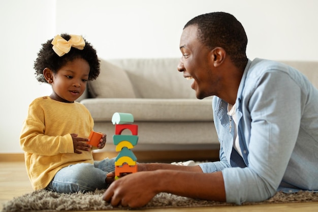 Um jovem pai negro alegre e amoroso a brincar com a sua filha.