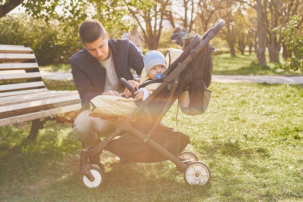 Um jovem pai passeando com um carrinho e um bebê em um parque de outono