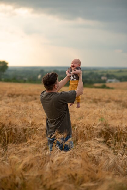 Um jovem pai segura seu filho de três meses nos braços. filmado em um campo de trigo.