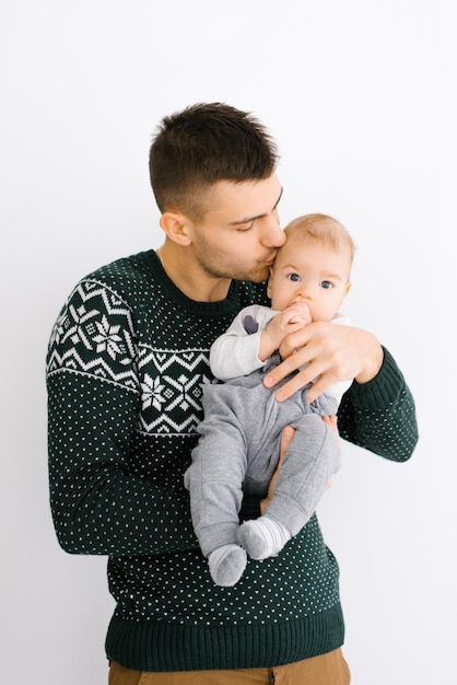 Foto um jovem pai segura seu filho em seus braços e o beija sobre um fundo branco