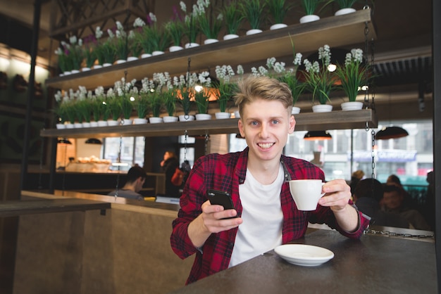 Um jovem positivo tem uma xícara de café nas mãos e olha para a câmera.