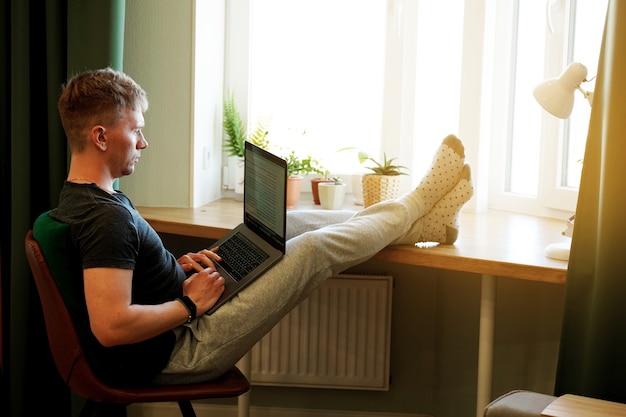 Um jovem programador trabalha usando um laptop em casa