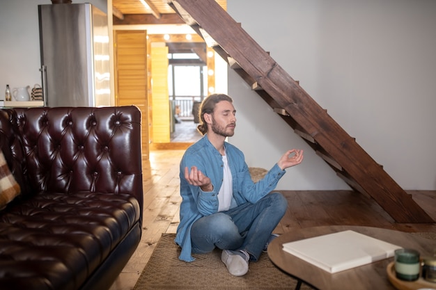 Um jovem relaxado meditando em seu apartamento