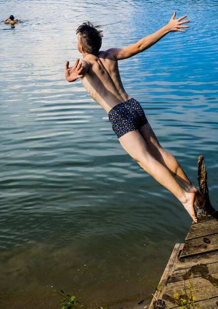 Um jovem sem camisa a saltar para o lago.