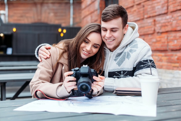 Um jovem sensual, muito elegante e sensual apaixonado, está sentado à mesa, tomando café e fazendo fotos com a câmera dslr ao ar livre no frio do inverno