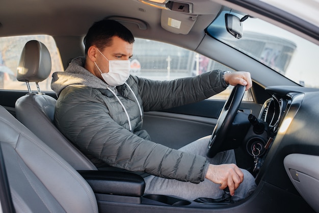 Um jovem senta-se ao volante usando uma máscara para segurança pessoal enquanto dirige durante uma pandemia e um coronavírus. epidemia