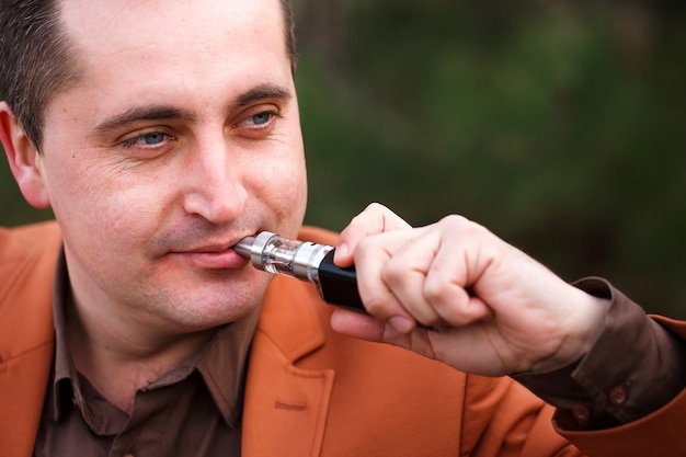 Um jovem senta-se em um banco e fuma um cigarro eletrônico.