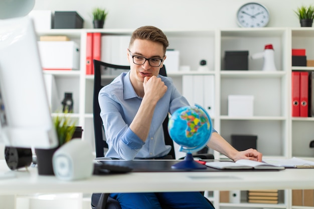 Um jovem senta-se no escritório em uma mesa de computador e na frente dele está um globo.