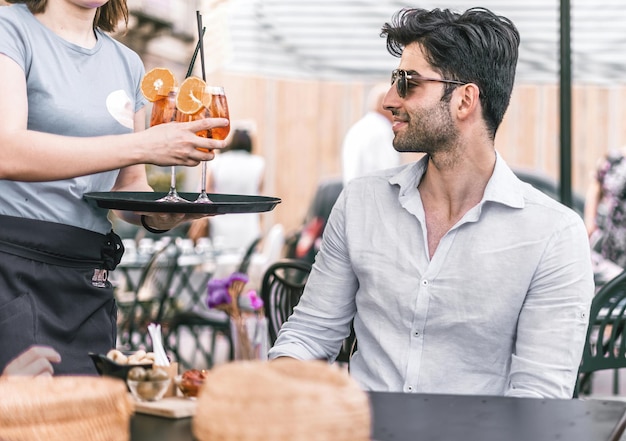 Um jovem sentado a uma mesa de bar recebe um coquetel do garçom