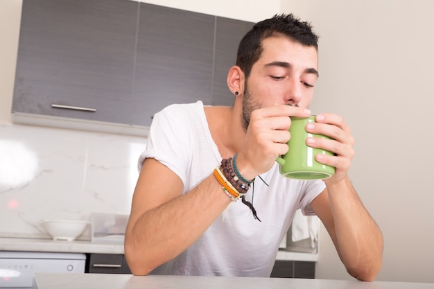 Um jovem sentado na cozinha e bebendo café.