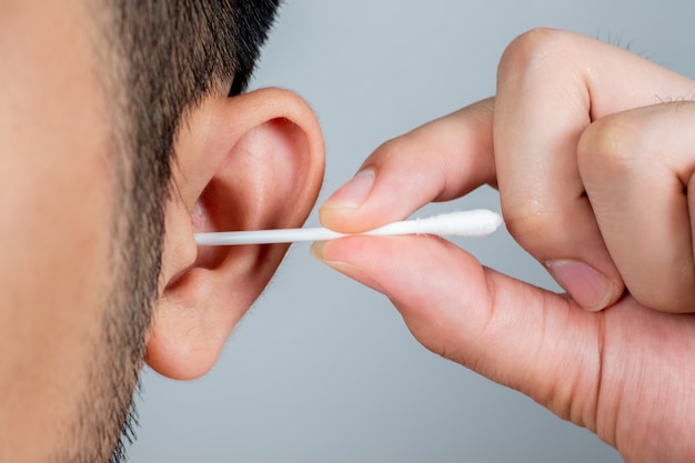 Um jovem Ásia usando um pedaço de cotonete para limpar as orelhas. Higiene diária.