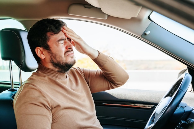 Foto um jovem sofredor está no carro e segura a mão na cabeça se contorcendo de dor a parada forçada atrasa o caso um problema comum para os motoristas é melhor parar