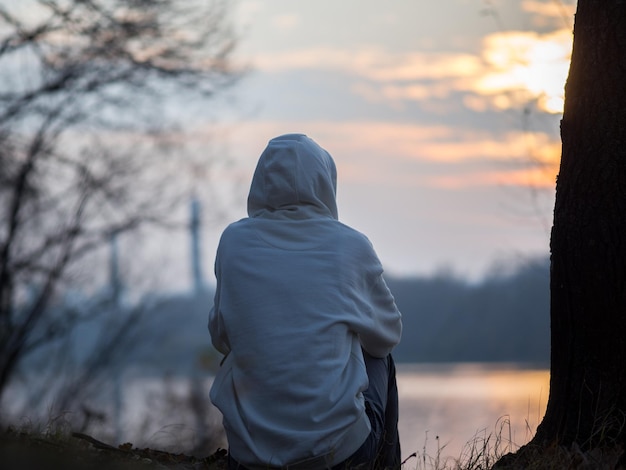 Foto um jovem solitário senta-se na margem do rio ao pôr do sol no outono humor depressivo melancólico da parte de trás