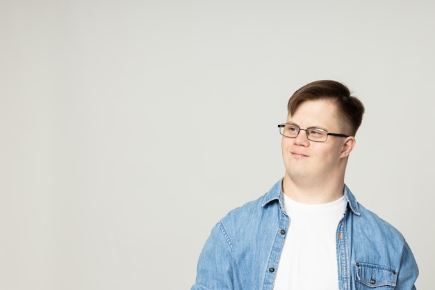 Um jovem sorridente com paralisia cerebral em jeans de óculos e uma camiseta branca posa para a câmera no Dia Mundial das Doenças Genéticas.