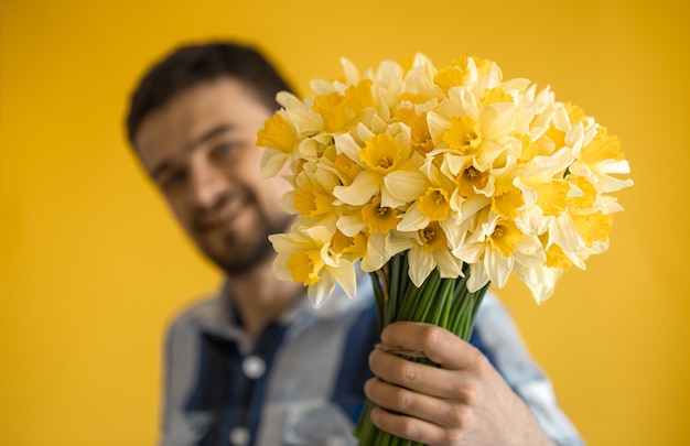 Um jovem sorridente com um buquê de flores da primavera em uma parede colorida