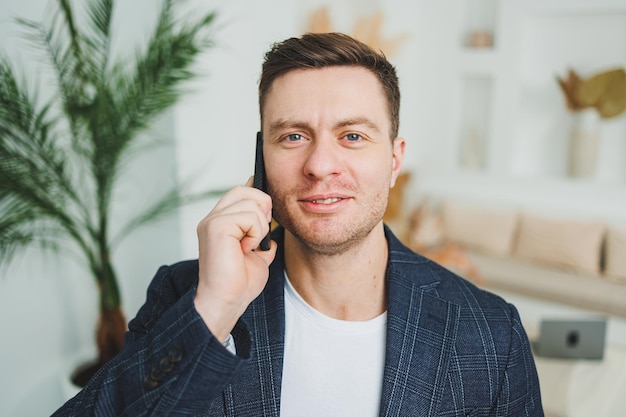 Um jovem sorridente de casaco está falando ao telefone Emoções de riso de falar ao telefone Um homem de sucesso trabalha remotamente no telefone