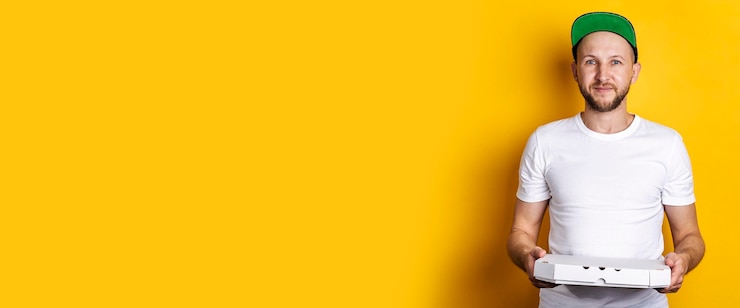 Foto um jovem sorridente em um boné de beisebol segura um pacote de pizza em um fundo amarelo banner
