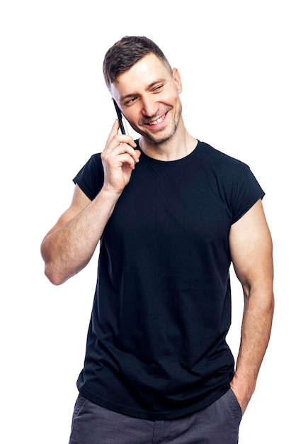 Um jovem sorridente em uma camiseta preta está falando ao telefone Isolado no fundo branco Vertical