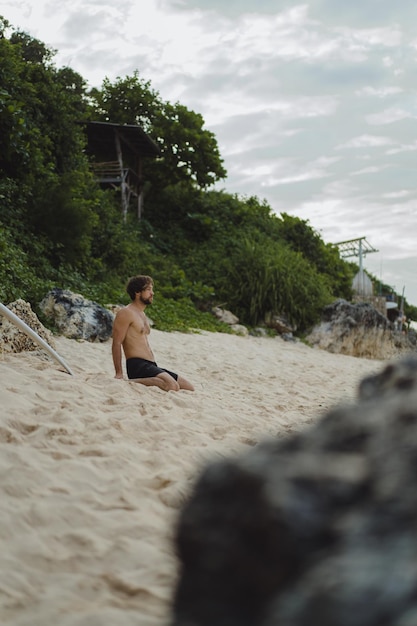 Um jovem surfista bonito na costa do oceano está fazendo um aquecimento antes de surfar. exercícios antes do esporte, alongamento antes do surf.