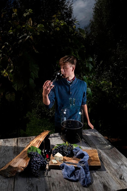 Um jovem testa vinho tinto caseiro de um copo no contexto de um vinhedo