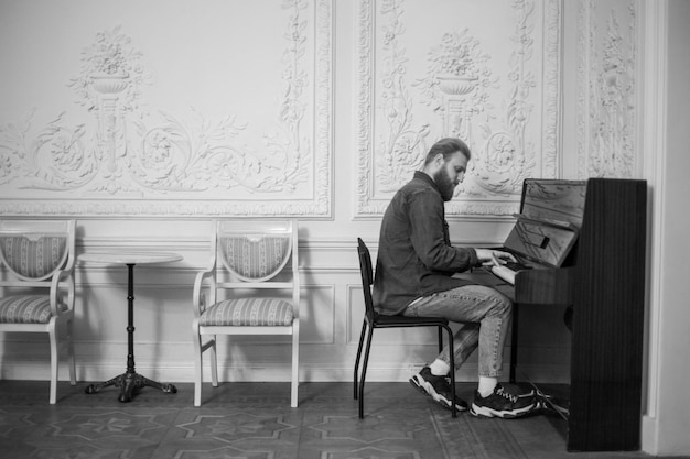 Um jovem toca piano em um grande salão branco preto e branco