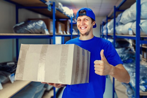 Um jovem trabalhador de armazém positivo segura uma caixa de papelão nas mãos e sorri