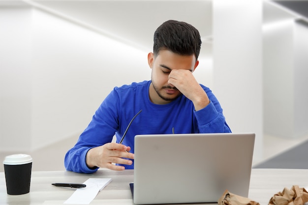 Um jovem trabalhando em um laptop. ele está com raiva e cansado. em branco isolado