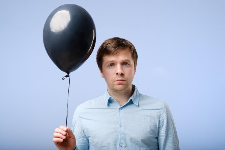 Foto um jovem triste de camisa azul está segurando um balão preto nas mãos luto e falta de vontade de festejar