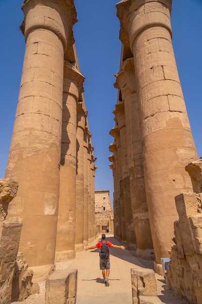 Foto um jovem turista ao lado das preciosas colunas com desenhos egípcios no templo de luxor, egito