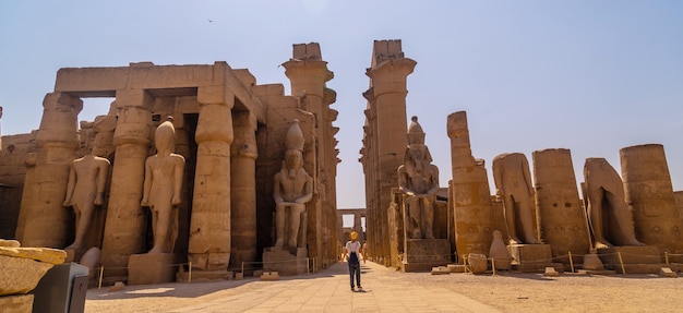 Um jovem turista de chapéu visitando o Templo Egípcio de Luxor e suas belas colunas