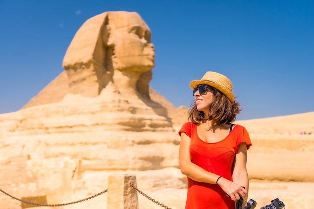 Foto um jovem turista na grande esfinge de gizé vestido de vermelho e com um chapéu