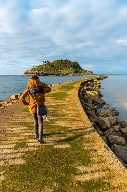 Foto um jovem turista na passarela para ir à ilha de san nicolas na maré baixa da praia de isuntza em lekeitio, país basco
