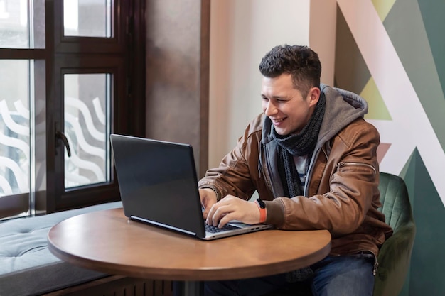 Um jovem usa um laptop enquanto está sentado em um café. Freelance. Trabalho remoto. Comunicações globais.