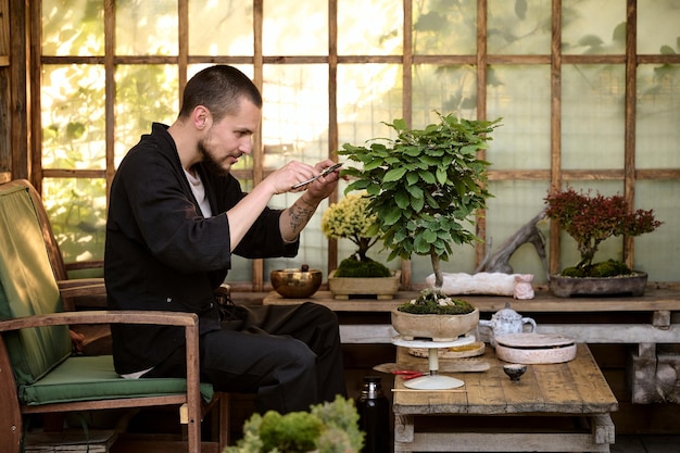 Foto um jovem usa uma tesoura para decorar os galhos de uma nova árvore bonsai em uma casa de jardim