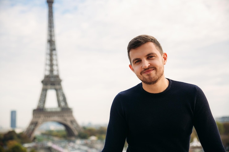 Foto um jovem vestindo uma jaqueta azul escura está de pé no fundo da torre eiffel o clima ensolarado é outono