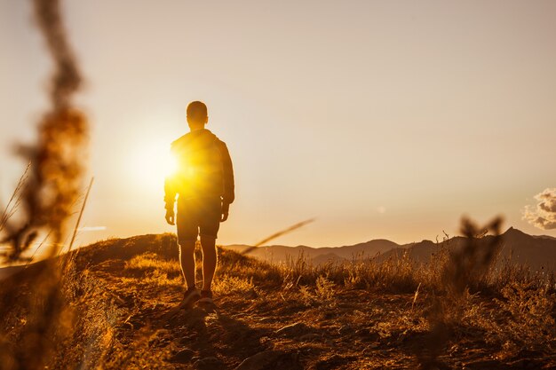 Um jovem viaja ao longo da costa da montanha ao pôr do sol Um homem está na encosta de uma montanha