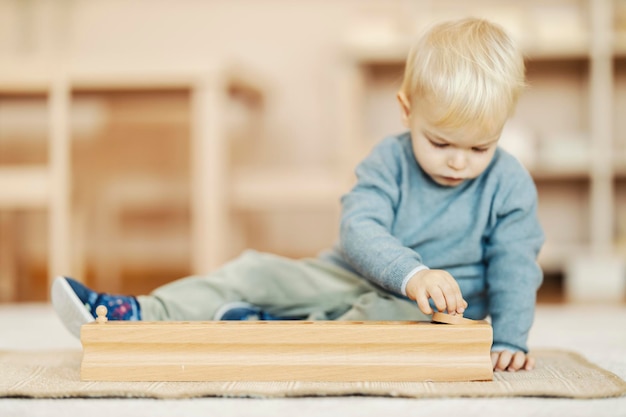 Um kindergartener fofo está brincando com formas com brinquedo montessori